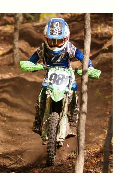 Tucker Aldrich #980 riding a wooded dirt trail on the Kawasaki